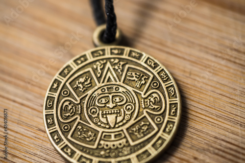 Aztec calendar amulet on a wooden background close-up.
