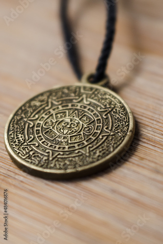 Aztec calendar amulet on a wooden background close-up.