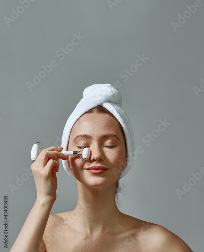 Girl in towel on head use beauty gua sha jade quartz roller for perfect glowing skin. Face lifting anti aging massage
