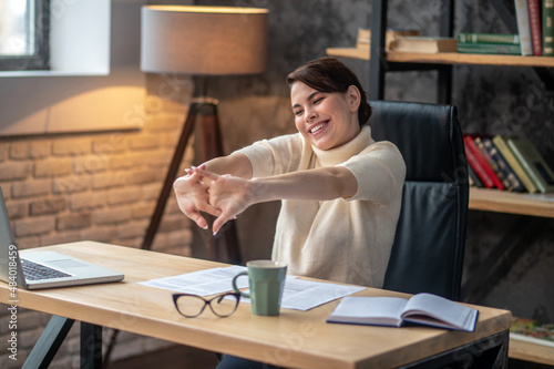Billede på lærred Joyous young woman cracking her knuckles at the desk