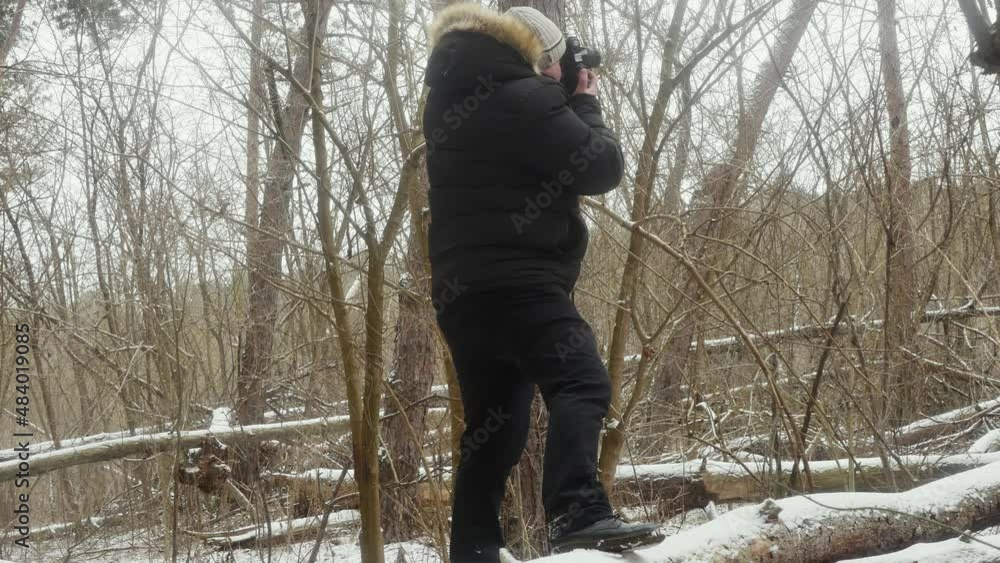 a traveler on a lying snow-covered tree photographs nature on a film camera