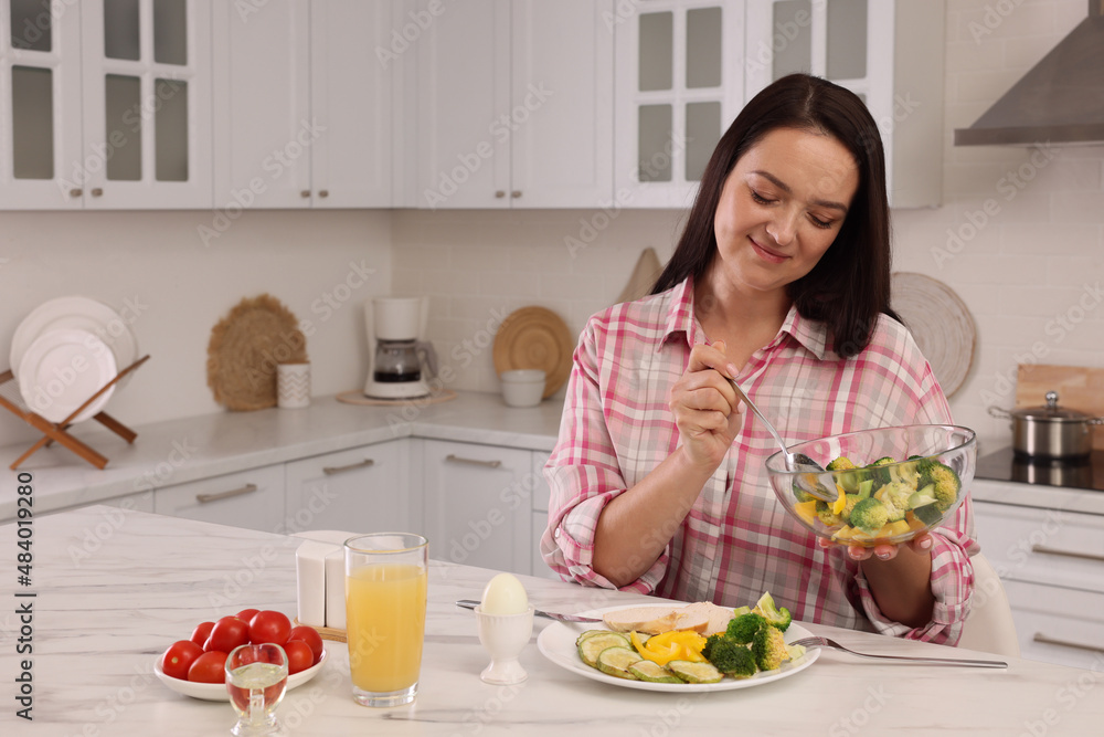 Beautiful overweight woman having healthy meal at table in kitchen