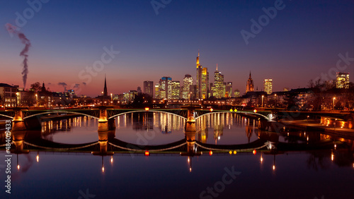 Skyline of Frankfurt am Main. Illuminated bridge with reflection in the water. Blue hour just after sunset.