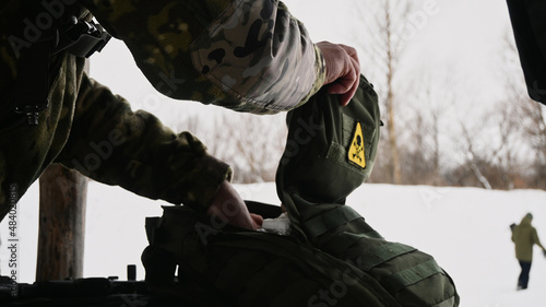 A soldier opens a backpack with a yellow skull and crossbones patch.