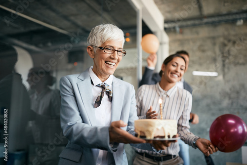 Konstfotografi Happy senior businesswoman carries Birthday cake on surprise party in the office