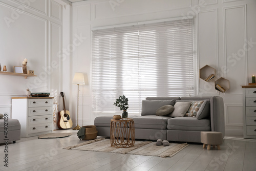 Living room with comfortable grey sofa and stylish interior elements near window