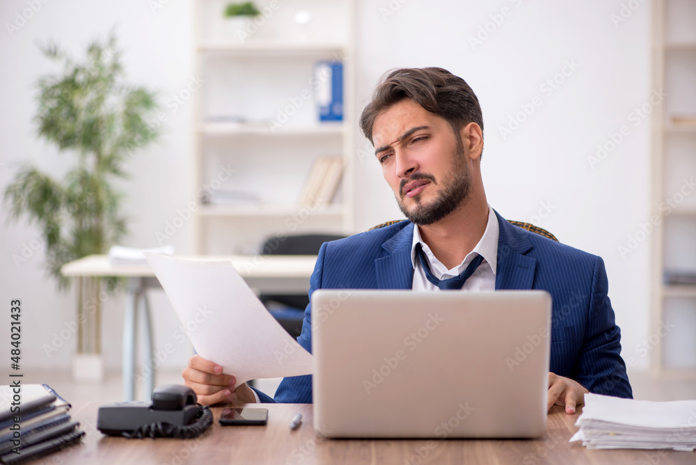 Young male employee unhappy with excessive work in the office Young male employee unhappy with excessive work in the office
