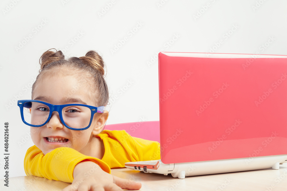 Portrait of beautiful playful little girl with glasses using laptop computer. Smiling nerd caucasian student studying online using notebook at home. Homeschooling, development and education concept. Portrait of beautiful playful little girl with glasses using laptop computer. Smiling nerd caucasian student studying online using notebook at home. Homeschooling, development and education concept.