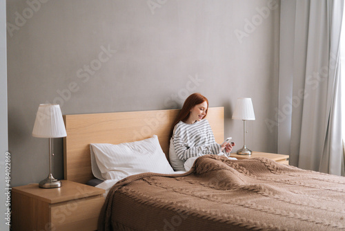 Remote view of happy young woman enjoy shopping online with credit card and mobile phone lying in bed at home. Smiling female holding credit card to make online payment at bedroom.