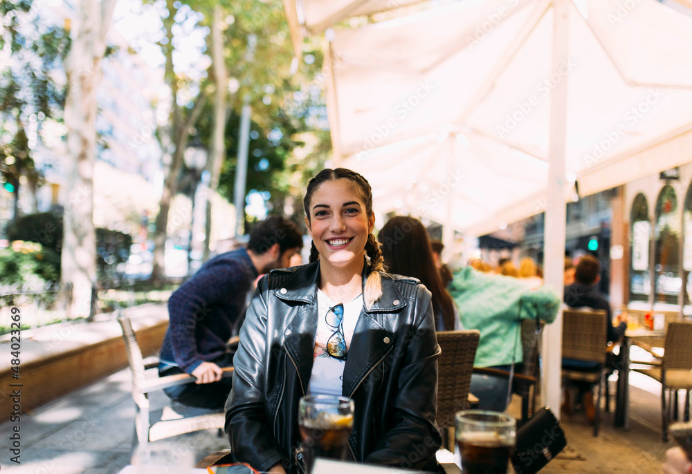 Happy young female sitting on a terrace of bar outdoors