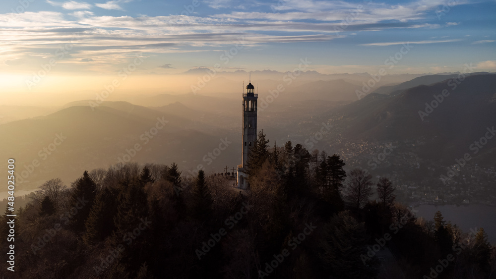 Aerial drone view of a lighthouse over Lake Como skyline with sunset light
