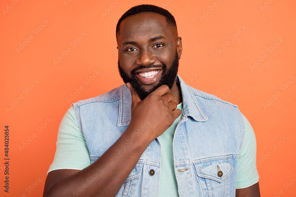 Photo of smart cute afro guy wear denim vest arm chin smiling isolated orange color background Photo of smart cute afro guy wear denim vest arm chin smiling isolated orange color background