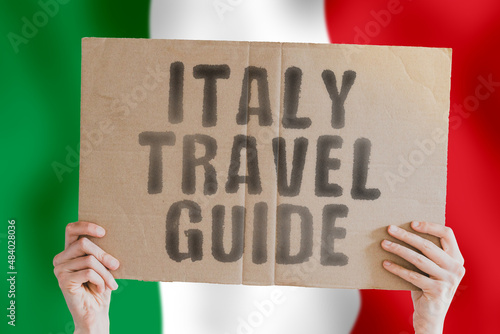 The phrase " Italy travel guide " on a banner in men's hand with blurred Italian flag on the background. Worldwide. Terminal. Schedule. Relax. Opportunity. Planet. Knowledge. Learn. Flying