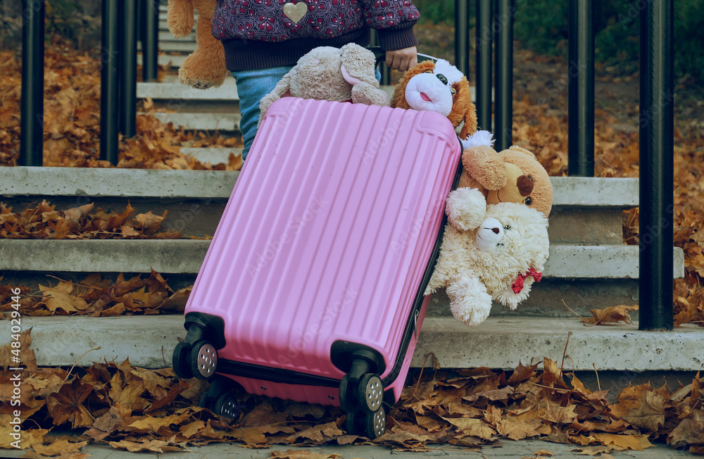 A pink suitcase with wheels stuffed with soft toys, climbs the concrete steps. Travel, personal belongings for walking