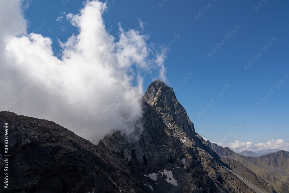 Clouds accumulating around the sharp mountain peaks of the Chaukhi massif in the Greater Caucasus Mountain Range in Georgia, Kazbegi Region. Mountain Ridges, Hiking. Georgian Dolomites. Cloudscape