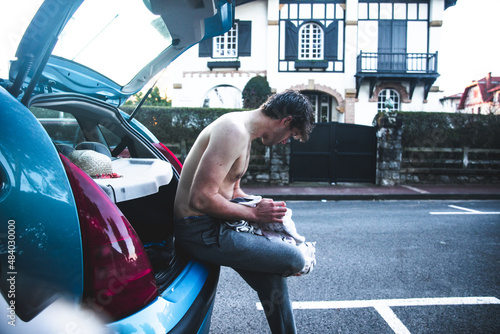 Photography Young caucasian man changing clothes on the car trunk after surfing at the beach