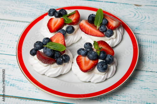 Four cakes Anna Pavlova with blueberries and strawberries with a mint leaf on a beautiful plate. Home confectionery. Old retro white and blue table.