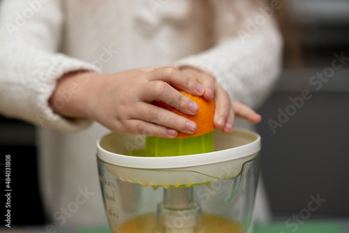 Two cute sister girls are making orange fresh juice.Hands close-up. They are in the kitchen at home. Family. Fresh fruit.