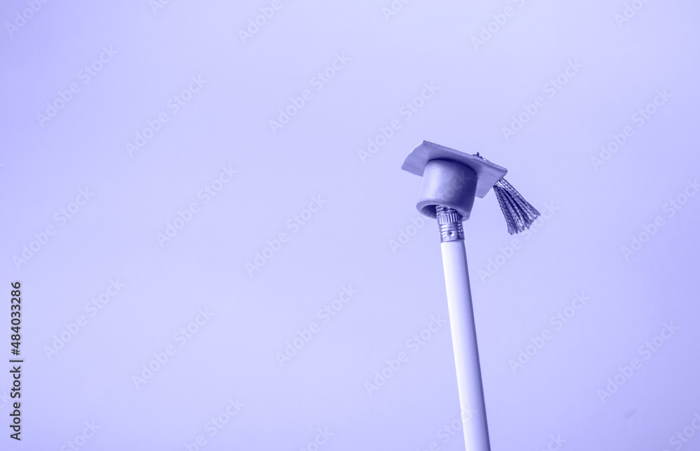 White pencil with graduation hat on a very peri background closeup with copy space. Education concept White pencil with graduation hat on a very peri background closeup with copy space. Education concept