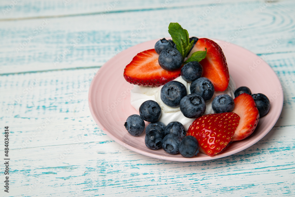 Pavlova cake with strawberries and blueberries and mint on a pink platter. Home confectionery. Old retro white and blue table. Pavlova cake with strawberries and blueberries and mint on a pink platter. Home confectionery. Old retro white and blue table.