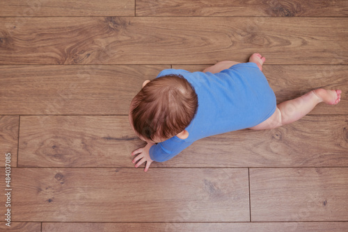 Happy baby toddler crawls on a wooden laminate. Funny child on the parquet in the home living room, aged 6-11 months
