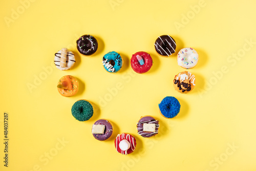 Colorful donuts or doughnuts in various shapes on yellow bright background. Colorful and happy image and concept.