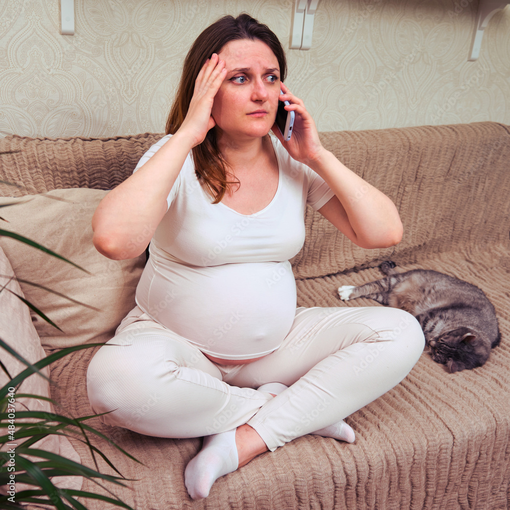 Pregnant woman calls an ambulance on the phone in the home interior Pregnant woman calls an ambulance on the phone in the home interior