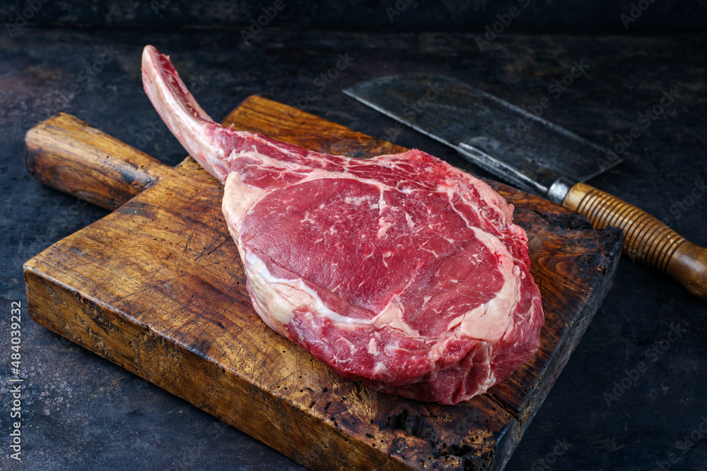 Raw dry aged chianina tomahawk steak offered as close-up with a cleaver on old rustic wooden board