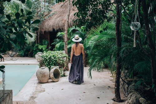 Girl in a luxury boutique hotel. Woman in sundress and hat walking in tropical jungle