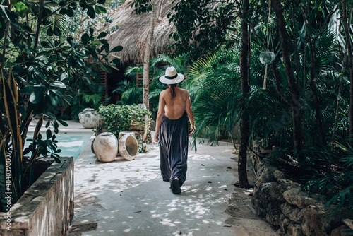 Girl in a luxury boutique hotel. Woman in sundress and hat walking in tropical jungle