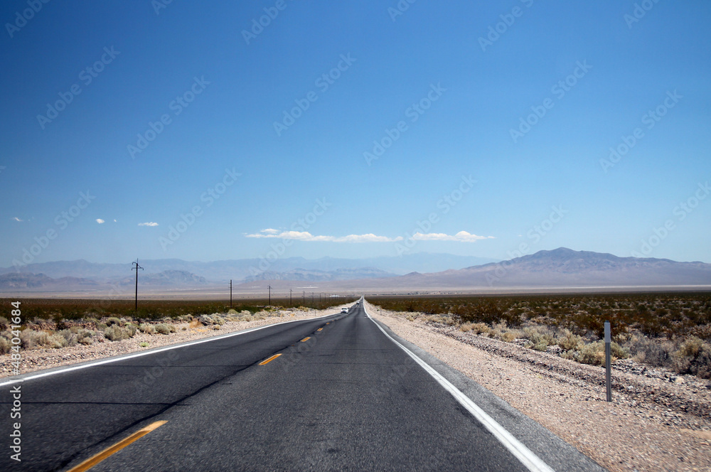 The Nevada Desert cut by a long infinite asphalt road under a clear blue sky