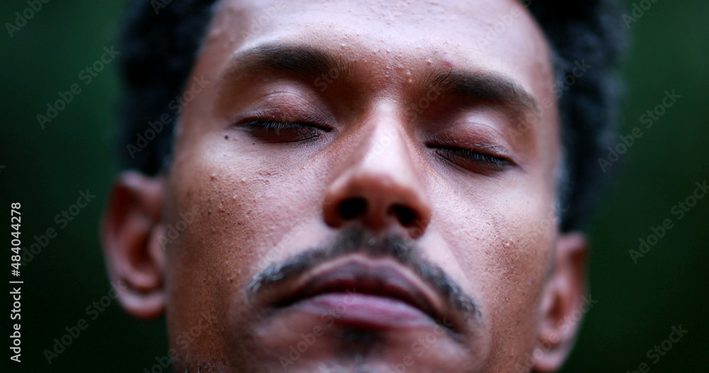 Black man meditating outside taking a deep breath and opening eyes to the sky, person contemplating life