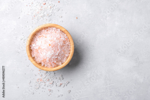 pink himalayan salt in a wooden bowl with scattered salt on a light grey background, copy space, top view, flat lay