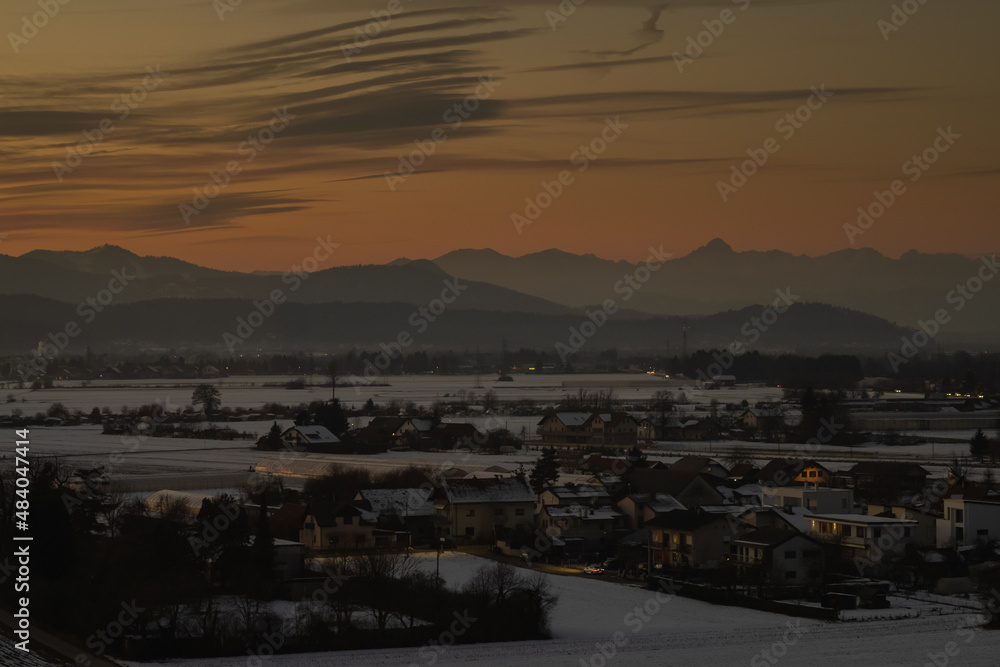 Panoramic view of houses on Savlje region of Ljubljana with visible magical yellow skies in the evening and julian alps with Triglav in the skyline.