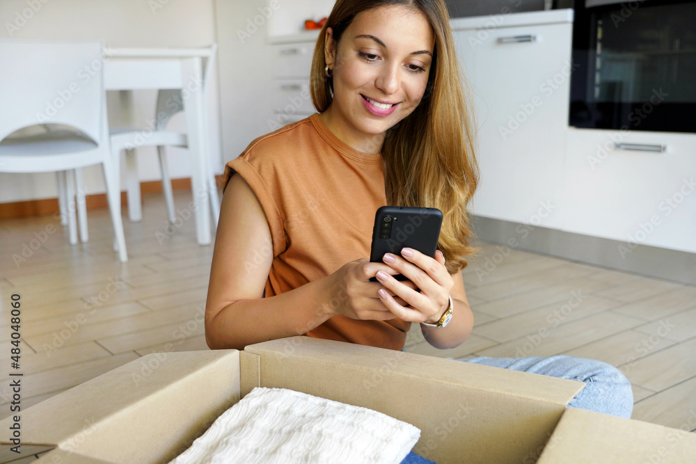 Online store selling clothes on website working on smartphone ecommerce business from home. Woman packing clothing purchase in shipping packages for delivery. Online store selling clothes on website working on smartphone ecommerce business from home. Woman packing clothing purchase in shipping packages for delivery.