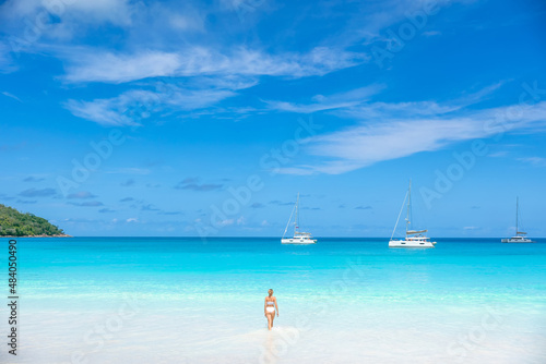 rear view of a girl in a white bathing suit  She stands in the sea and looks at the yacht