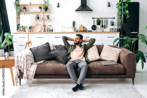 Obraz na plátne Satisfied relaxed young indian man chilling on sofa in living room, smiling