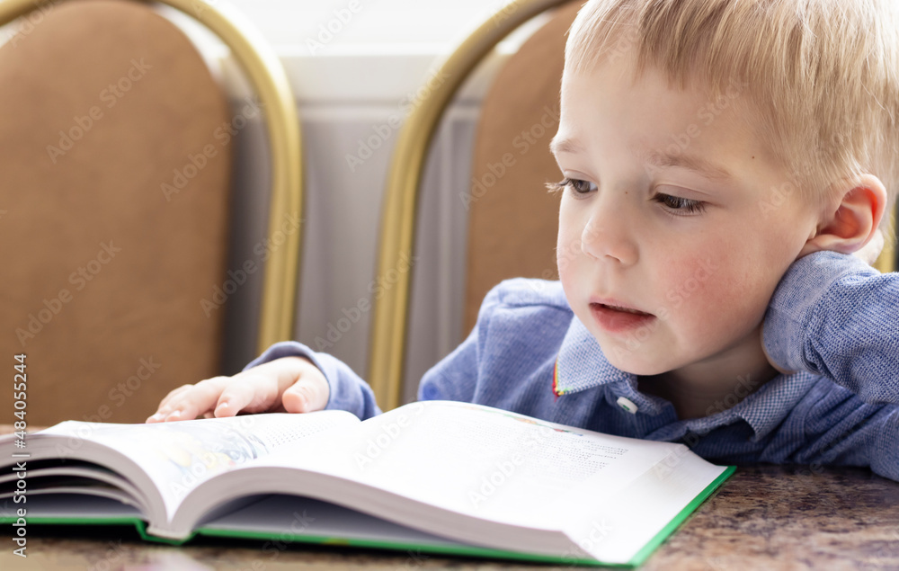 close-up of a pensive blond-haired toddler leaning over a book holding his head close-up of a pensive blond-haired toddler leaning over a book holding his head