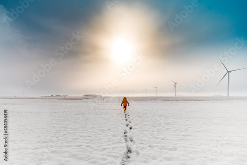 a boy running through snow during sunrise on a wind farm photo