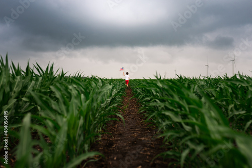 a boy walking through a corn field with a flag on a cloudy day photo