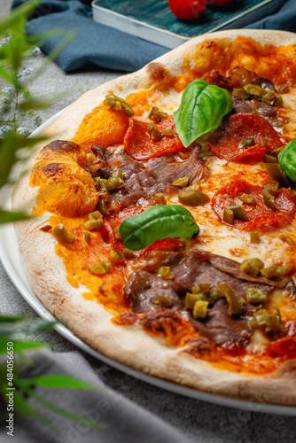 Traditional Italian pizza "Pescara" with Parma ham, arugula, olives, basil, mozzarella cheese, grana padano cheese on a plate on a gray stone table. Restaurant Menu