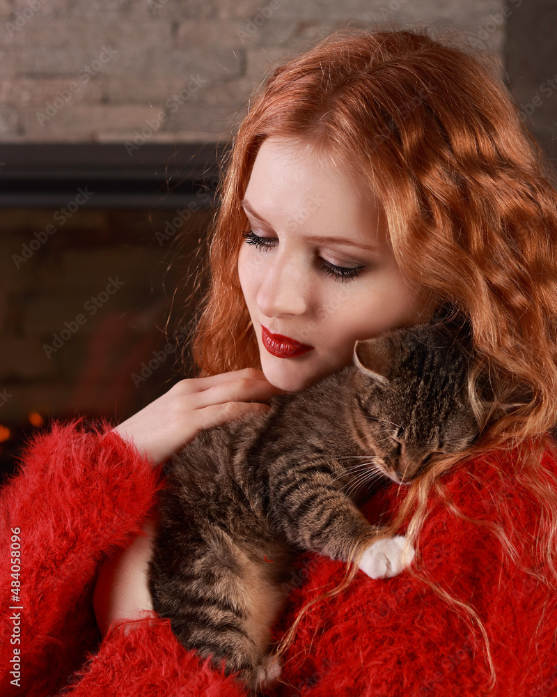 Attractive young Woman resting by the fireplace and a small Kitten. Beautiful Woman. Comfort. Cat on a background of fire in the fireplace. Striped Kitten sitting in the arms of a beautiful Girl Attractive young Woman resting by the fireplace and a small Kitten. Beautiful Woman. Comfort. Cat on a background of fire in the fireplace. Striped Kitten sitting in the arms of a beautiful Girl