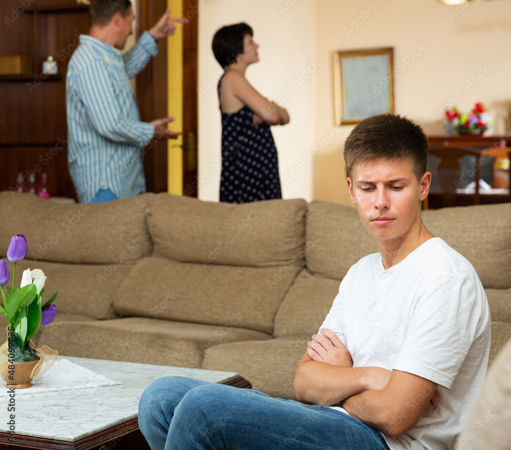 Adult spouses quarrelling while their teenage son sitting offended on sofa