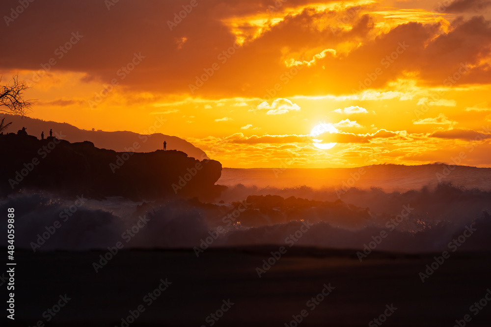 Perfect warm summer sunset at the beach with big waves and clouds with a silhouette of a man staying on the cliff