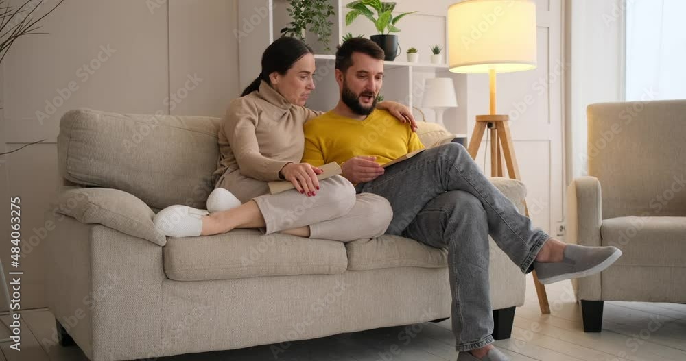 Couple reading book and discussing sitting on sofa at home Couple reading book and discussing sitting on sofa at home