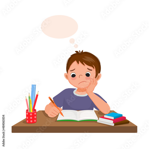 little boy feeling tired, bored and lazy studying, doing his homework at the desk at home