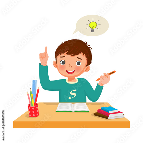 Little boy got an idea to solve the problems in math homework raised his finger pointing up while sitting studying on the desk at home