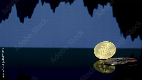Three physical bitcoin coins on a reflective black surface, with a price drop chart