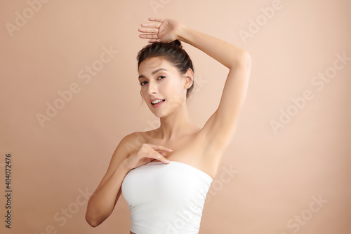 Beautiful Young Asian woman lifting hands up to show off clean and hygienic armpits or underarms on beige background, Smooth armpit cleanliness and protection concept photo