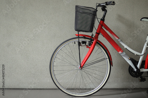 Close-up of bicycle front wheel with basket in front of gray wall with copy space